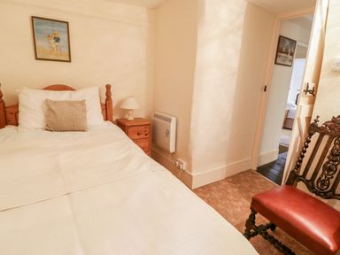 A bedroom with a single bed bedside table lamp chair and a painting on the wall at 2 Rose Cottages Lansallos near Polperro