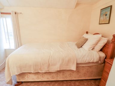 A bedroom with a wooden bed frame white bedding a small window and a wooden nightstand at 2 Rose Cottages Lansallos near Polperro