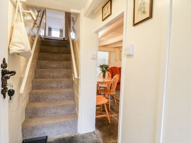 A stairway with carpeted steps and white handrails next to a room with a round wooden table and chairs at 2 Rose Cottages Lansallos near Polperro