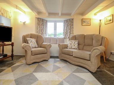 A living room with beige sofas a patterned rug and a television at 2 Rose Cottages Lansallos near Polperro