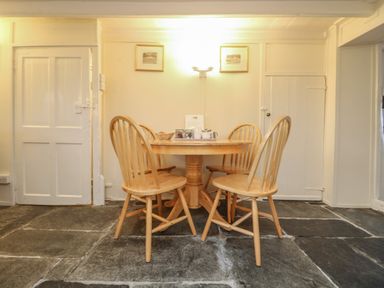 A dining area with a round wooden table and four wooden chairs on a stone tile floor at 2 Rose Cottages Lansallos near Polperro