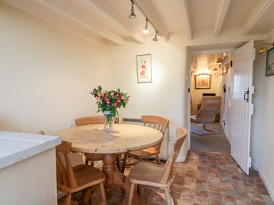 A dining area with a round wooden table and four chairs with flowers on the table at 3 Rose Cottages Lansallos near Polperro