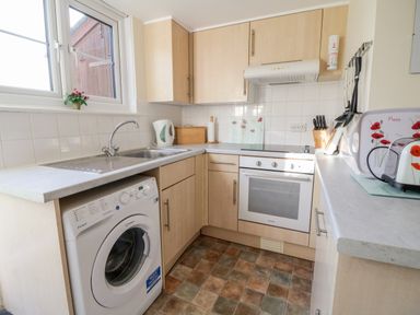 A small kitchen with a washing machine sink oven and wooden cabinets at 3 Rose Cottages Lansallos near Polperro