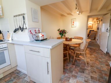 A kitchen and dining area with a round wooden table and chairs and a toaster on the counter at 3 Rose Cottages in Lansallos near Polperro