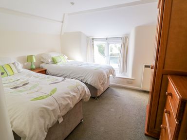 A bedroom with two single beds a bedside table with a lamp a window and wooden wardrobes at 3 Rose Cottages in Lansallos near Polperro