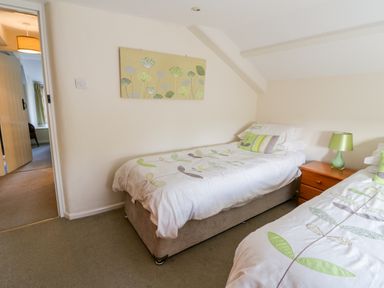 A bedroom with two single beds a wooden nightstand and a lamp at 3 Rose Cottages Lansallos near Polperro