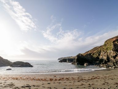 A sandy beach with seaweed and rocky cliffs by the ocean under a blue sky at 3 Rose Cottages Lansallos near Polperro