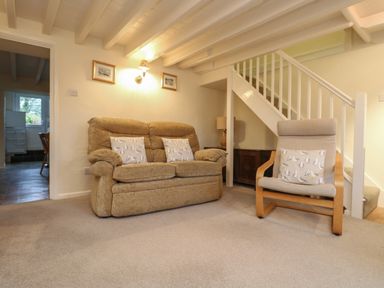 A living room with a beige sofa and armchair near a staircase at 3 Rose Cottages in Lansallos near Polperro