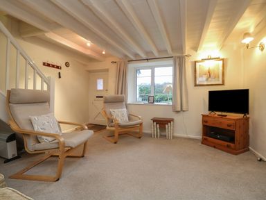 A living room with two armchairs a TV on a wooden stand and a window at 3 Rose Cottages Lansallos near Polperro
