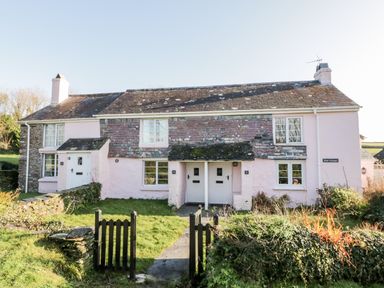 A pink stone cottage with two white doors and a small garden behind a black gate at 4 Rose Cottages in Lansallos near Polperro
