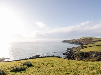 A coastal landscape with grassy cliffs and the ocean at 4 Rose Cottages Lansallos near Polperro