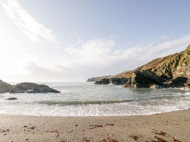 A sandy beach with seaweed and rocks along the shore and cliffs in the distance at 4 Rose Cottages in Lansallos near Polperro