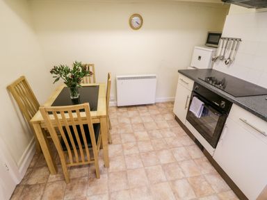 A kitchen with a wooden dining table and four chairs a stove an oven a microwave and kitchen utensils at 4 Rose Cottages Lansallos near Polperro