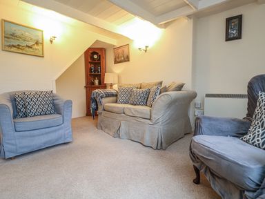 A living room with armchairs sofa cushions a corner cabinet and framed pictures on walls at 4 Rose Cottages Lansallos near Polperro