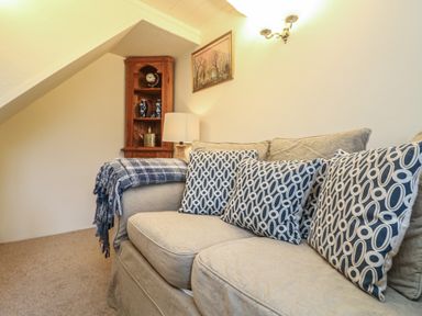 A living room with a couch patterned cushions a wooden corner shelf and a wall lamp at 4 Rose Cottages in Lansallos near Polperro