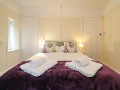 A bedroom with a double bed two pillows with floral pattern and rolled towels on a purple blanket at 4 Rose Cottages in Lansallos near Polperro