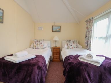 A bedroom with two single beds with purple throws and flower patterned pillows at 4 Rose Cottages Lansallos near Polperro
