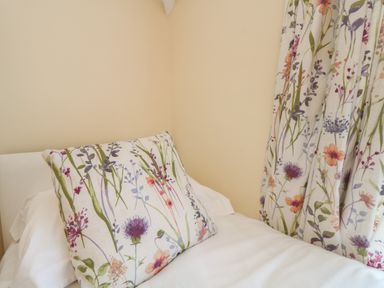 A bed with a floral patterned cushion and matching curtains at 4 Rose Cottages Lansallos near Polperro