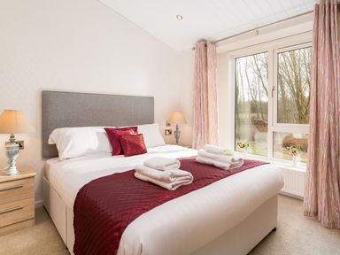 A bedroom with a double bed bedside tables lamps and windows with curtains at Waternook Lodge in South Lakeland Leisure Village