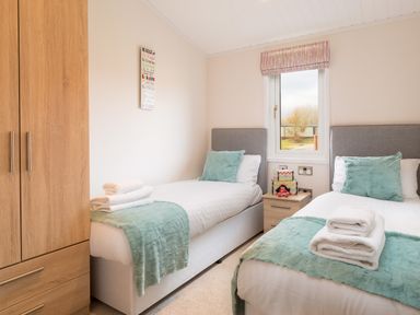 A bedroom with two single beds a wooden wardrobe and a window at Waternook Lodge South Lakeland Leisure Village