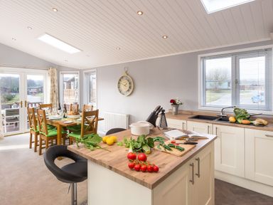 A kitchen and dining area with a wooden dining table set and kitchen island with vegetables at Waternook Lodge South Lakeland Leisure Village