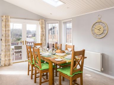 A dining room with a wooden table set for six people and glass doors at Waternook Lodge South Lakeland Leisure Village