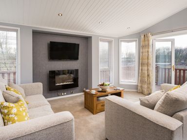 A living room with two sofas a coffee table a wall-mounted tv and a fireplace at Waternook Lodge South Lakeland Leisure Village