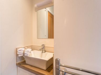 A bathroom sink with folded towels on a wooden countertop and a mirror above at Waternook Lodge South Lakeland Leisure Village