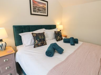 A bedroom with a double bed white bedding teal headboard bedside tables lamps and towels at The Cwtch in St Brides Major