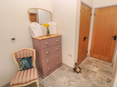 A hallway with a chest of drawers mirror chair and wooden doors at The Cwtch in St Brides Major