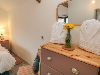 A bedroom corner with a wooden dresser holding folded white robes and a vase with yellow flowers at The Cwtch in St Brides Major