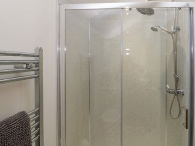 A shower cabin with two shower heads and a towel rack with a brown towel in a bathroom at The Cwtch in St Brides Major