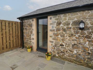 A stone exterior wall with a glass door two yellow flower pots on the ground and a wooden fence at The Cwtch in St Brides Major