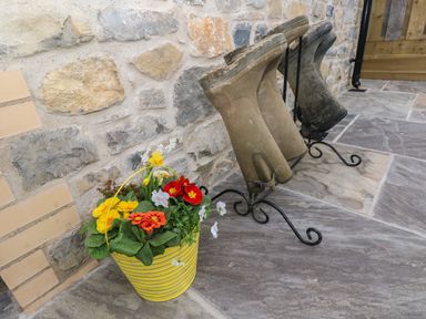 A stone wall with three rubber boots on stands next to a yellow bucket with flowers at The Cwtch in St Brides Major
