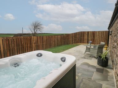 An outdoor patio with a hot tub table and two chairs next to a wooden fence and stone wall at The Cwtch in St Brides Major