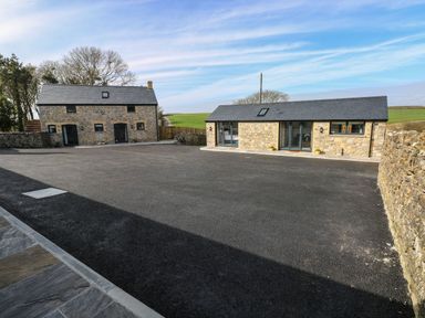 Two stone buildings with slate roofs and large paved area surrounded by low stone walls at The Cwtch in St Brides Major