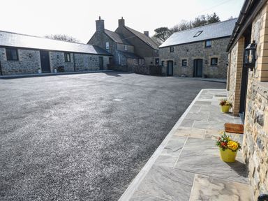 An outdoor courtyard with stone buildings and yellow flower pots at The Cwtch in St Brides Major