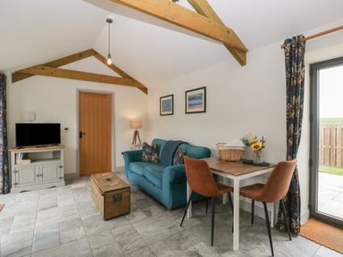 A living room with a teal sofa a wooden chest used as a coffee table a small dining table with two chairs and a TV on a cabinet at The Cwtch in St Brides Major