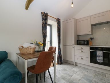 A kitchen with beige cabinets a table with two brown chairs a dark green sofa and a door with patterned curtains at The Cwtch in St Brides Major