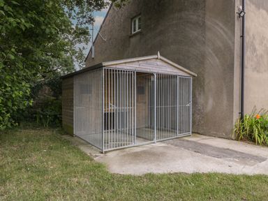 An outdoor wooden enclosure with metal bars attached to the side of a building with grass and plants nearby at The Cwtch in St Brides Major