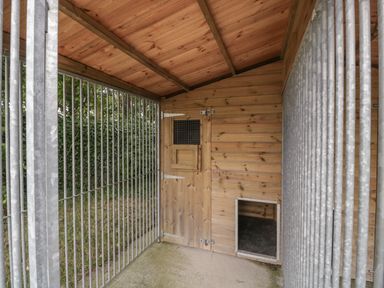 An outdoor wooden dog kennel with metal bars and a small door at The Cwtch in St Brides Major