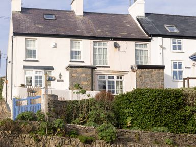 A white stone house with slate roof and blue gate surrounded by greenery at Old Post Office in Bull Bay