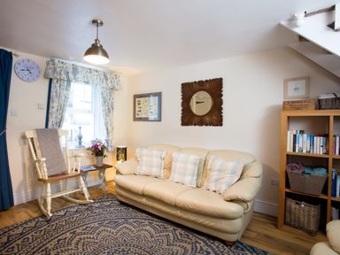 A living room with a cream sofa and rocking chair near a window with curtains at Old Post Office in Bull Bay