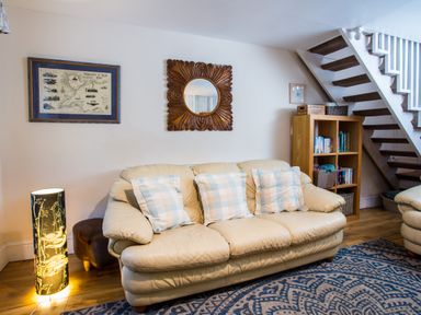 A living room with a beige sofa and three checkered pillows a wooden bookshelf under stairs a standing lamp and wall decorations at Old Post Office in Bull Bay