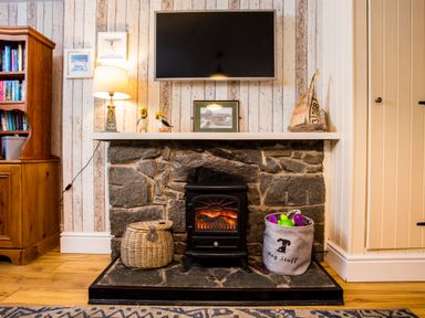 A stone fireplace with a small stove and baskets on each side below a mounted television and lamp in a sitting room at Old Post Office Bull Bay