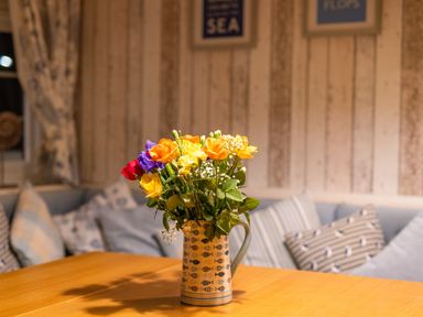 A bouquet of flowers in a patterned jug on a wooden table in a room with cushions on a sofa at Old Post Office in Bull Bay