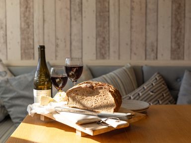 A loaf of bread with a knife on a wooden board with two glasses of red wine and a wine bottle on a table at Old Post Office in Bull Bay