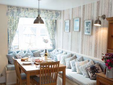 A dining area with wooden table and chairs cushions on bench and framed pictures on wall at Old Post Office in Bull Bay