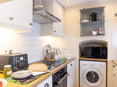 A kitchen with a toaster bread jar plates stove microwave washing machine and shelves at Old Post Office Bull Bay