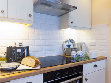 A kitchen countertop with sliced bread, a toaster, plates, a jar, two mugs, a teapot, a kettle, and jars at Old Post Office Bull Bay